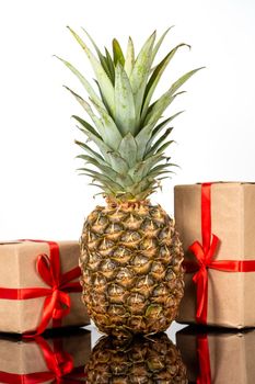 Fresh pineapple fruit and square gift boxes in craft paper on black glass table on white background