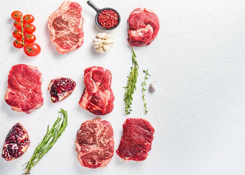 Rraw beef steaks set top blade, rump, chuck eye roll with herbs pomegranate over white concrete background, top view space for text