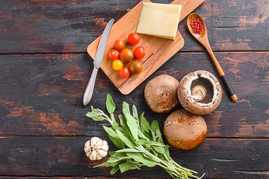 Portabello mushrooms ingredients for baking, cheddar cheese, cherry tomatoes and sage on old dark wood background, top view space for text