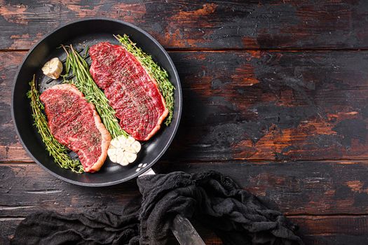Two raw picanha organic beef steaks ready for grill on pan with herbs and garlic. Over old dark wooden background, top view with space for text