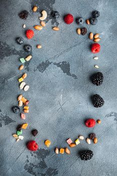 Frame made of mixed dried and raw ripe berry and fruit with nuts, top view with copy space, on grey background