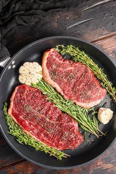Two raw picanha organic beef steaks ready for grill on pan with herbs and garlic. Over old dark wooden background, top view