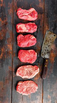 A set of different types of raw beef steaks:top blade, rump, chuck eye roll over old wooden background top view with butcher cleaver