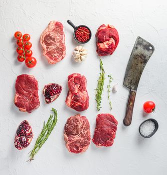 Rraw beef steaks set top blade, rump, chuck eye roll with herbs pomegranate and butcher knife for chopping over white concrete background, top view