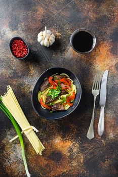 Chinese noodles with vegetables and beef in black bowl top view.