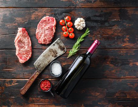 Organic top blade steak, raw beef meat with seasonings, rosemary and butcher cleaver and red wine bottle. Wood textured background. Top view panorama space for text