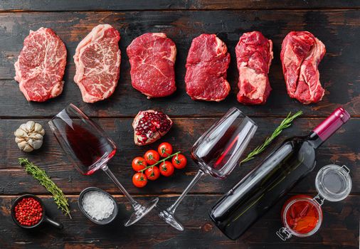 Organic alternative beef cuts top blade steak, chuck roll, rump steak raw beef meat with seasonings, rosemary and butcher cleaver and red wine bottle. Wood textured background. Top view panorama big size