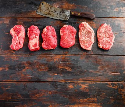 A set of different types of raw beef steaks:top blade, rump, chuck eye roll over old wooden background top view space for text
