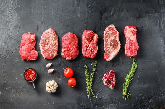 Variety of raw alternative steaks picanha, ramp and chuck eye roll and top blade with herbs for grill over black background top view. Big size. Space for text