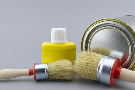 New color, decorating or renovations concept with a still life with assorted clean paint brushes and unlabeled tin of paint over a grey background