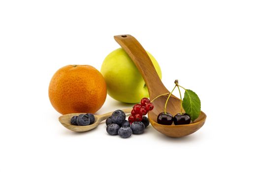 Fresh seasonal berries including blueberries, cherries and red currants, wooden spoons, apple and orange on a white background