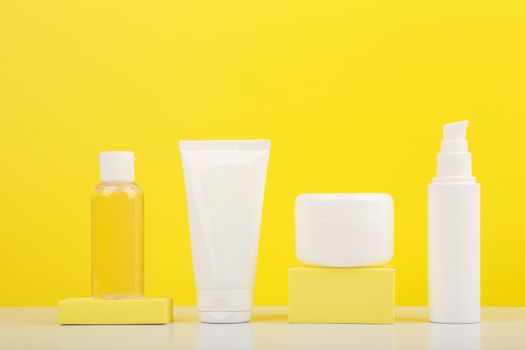 Still life with set of cosmetic containers on white glossy table against bright yellow background. . Concept of everyday skin care for smooth, young looking skin