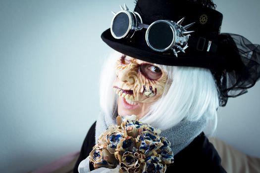 Woman with monster face and black hat wearing steampunk glasses. White hair.