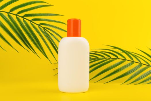 Minimalistic still life with unbranded sunscreen lotion with two palm leaves at the sides against yellow background. Concept of safe tan and summer holidays by sea