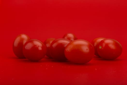 Still life with bunch of wet tomatoes with water drops against red background with copy space. Concept of cooking, healthy eating or vegan food