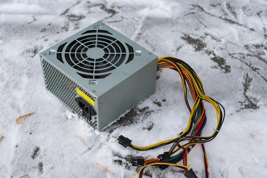 An old computer power supply discarded in the snow in winter