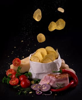 Potato chips on a dark wooden board. Fast food. Dark background. Top view