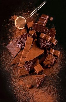 Broken chocolate pieces and cocoa powder on wooden background