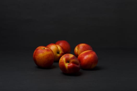 Still life with bunch of nectarines on black table against black background with copy space. High quality photo