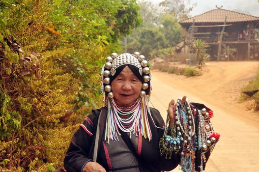 CHIANG MAI, THAILAND - MARCH 1, 2013: Mature ethnic woman with traditional attire in authentic gown and headwear holding heap of traditional adornments in village. Noth tribes Akha, Lisu, Karen, Lahu
