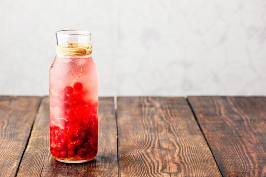 Red currant infused water with ice in glass bottle
