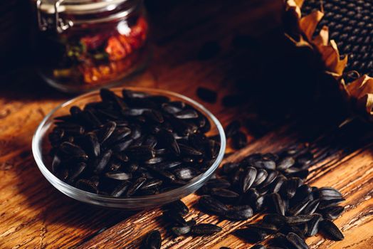 Roasted seeds on the glass saucer and dried sunflower over old wooden surface