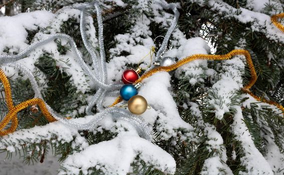 Christmas composition. Christmas tree branch in the snow with toys and tinsel . Snow spruce branch in the forest. Russian winter landscape. Space for your text.