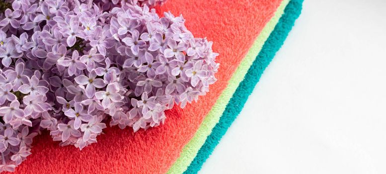 A stack of colorful bath towels with a sprig of lilac on a light background. Hygiene, fabric, spa and textile concept.