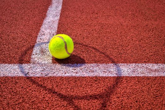 Shadows of net and racket surrounding a tennis ball on a white line on an outdoor court in sunshine in a sport and active lifestyle concept