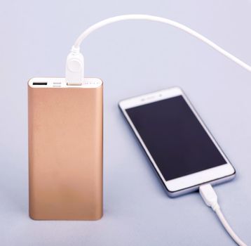 Smartphone charging with power bank and phone on gray background.