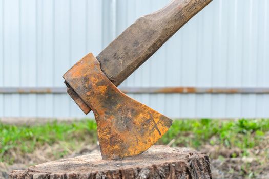 An old and rusty ax sticks out of an old tree stump