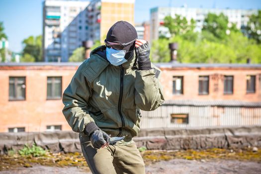 A masked criminal with a knife in his hands is trying to hide from pursuit