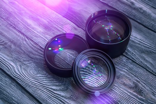 A set of photo lenses lying on a wooden table in the dark illuminated by the light of multi-colored lamps