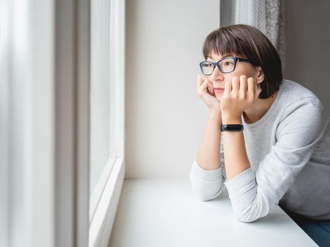 Sad woman looks at the window. Forced stay at home because of coronavirus COVID19 quarantine pandemic.