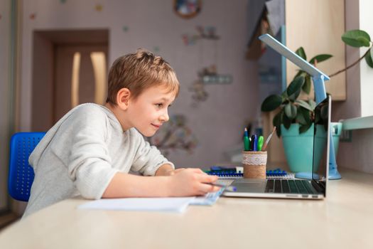 Cute little schoolboy studying at home doing school homework. Training books and notebook on the table. Distance learning online education