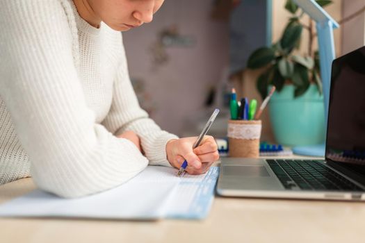 Beautiful schoolgirl studying at home doing school homework. Hand's close-up. Training books and notebook on the table. Distance learning online education