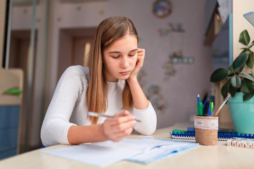 Beautiful tired schoolgirl studying at home doing school homework. Training books and notebook on the table. Distance learning online education