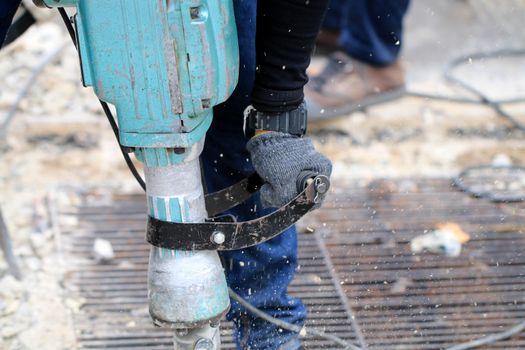 Male workers use electric concrete breaker for digging and drilling concrete repairing driveway surface with jackhammer at the local city road, during sidewalk, work construction site.