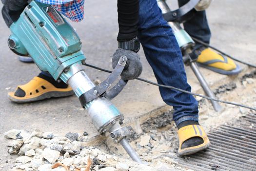 Male workers use electric concrete breaker for digging and drilling concrete repairing driveway surface with jackhammer at the local city road, during sidewalk, work construction site.