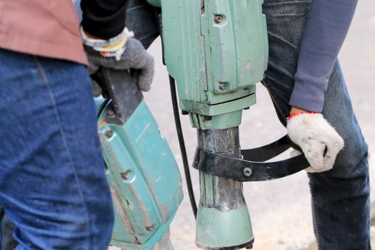 Male workers use electric concrete breaker for digging and drilling concrete repairing driveway surface with jackhammer at the local city road, during sidewalk, work construction site.