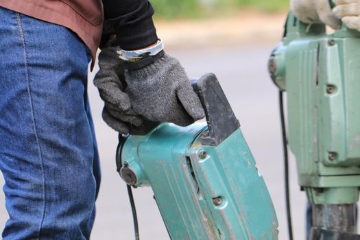 Male workers use electric concrete breaker for digging and drilling concrete repairing driveway surface with jackhammer at the local city road, during sidewalk, work construction site.