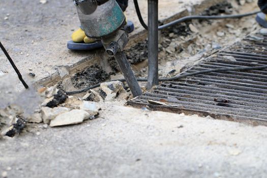 Male workers use electric concrete breaker for digging and drilling concrete repairing driveway surface with jackhammer at the local city road, during sidewalk, work construction site.