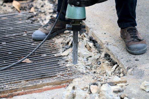 Male workers use electric concrete breaker for digging and drilling concrete repairing driveway surface with jackhammer at the local city road, during sidewalk, work construction site.