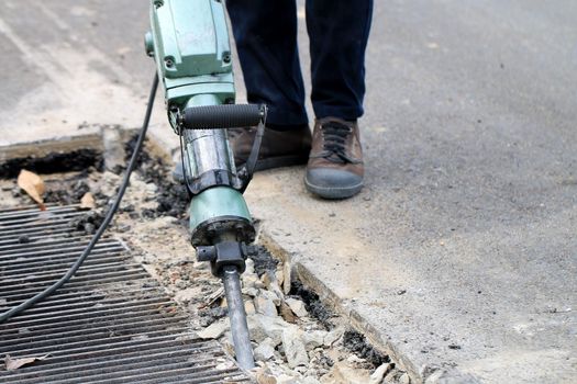 Male workers use electric concrete breaker for digging and drilling concrete repairing driveway surface with jackhammer at the local city road, during sidewalk, work construction site.