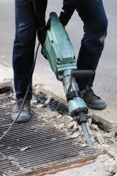 Male workers use electric concrete breaker for digging and drilling concrete repairing driveway surface with jackhammer at the local city road, during sidewalk, work construction site.