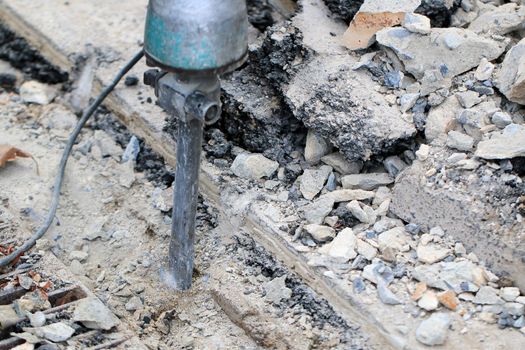 Male workers use electric concrete breaker for digging and drilling concrete repairing driveway surface with jackhammer at the local city road, during sidewalk, work construction site.