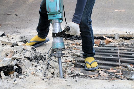 Male workers use electric concrete breaker for digging and drilling concrete repairing driveway surface with jackhammer at the local city road, during sidewalk, work construction site.