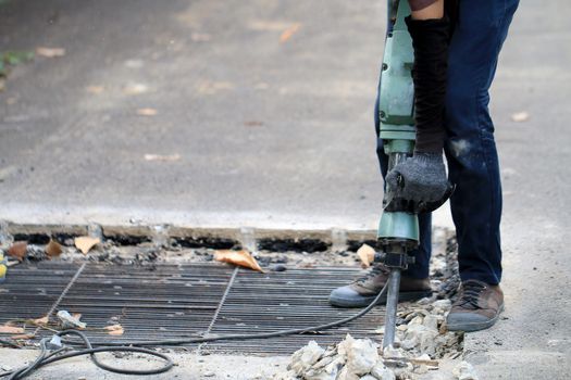 Male workers use electric concrete breaker for digging and drilling concrete repairing driveway surface with jackhammer at the local city road, during sidewalk, work construction site.