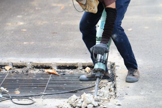 Male workers use electric concrete breaker for digging and drilling concrete repairing driveway surface with jackhammer at the local city road, during sidewalk, work construction site.