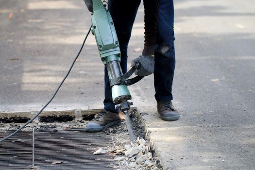 Male workers use electric concrete breaker for digging and drilling concrete repairing driveway surface with jackhammer at the local city road, during sidewalk, work construction site.